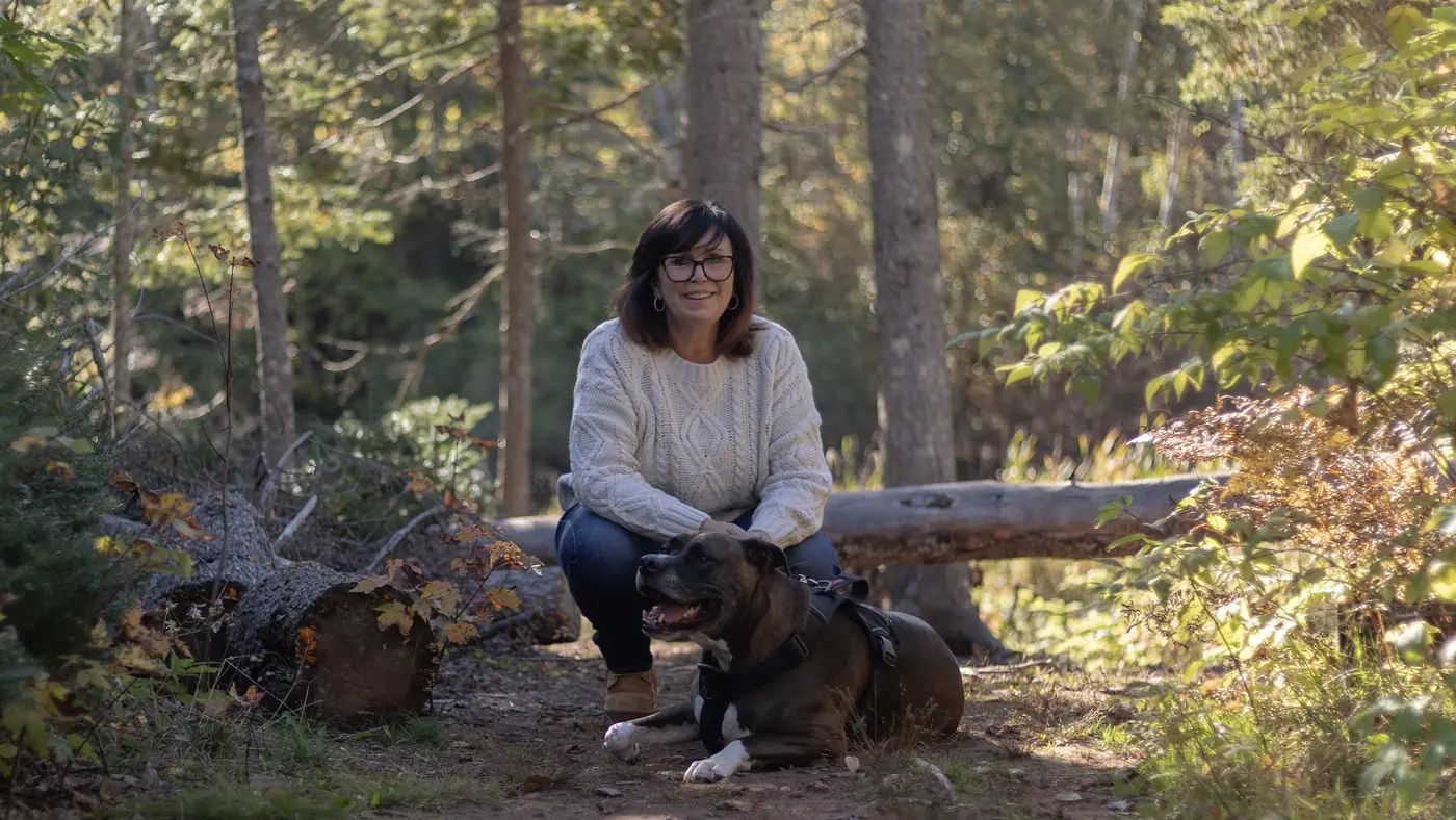 Kim crouching beside her dog Frankie on a wooded autumn trail