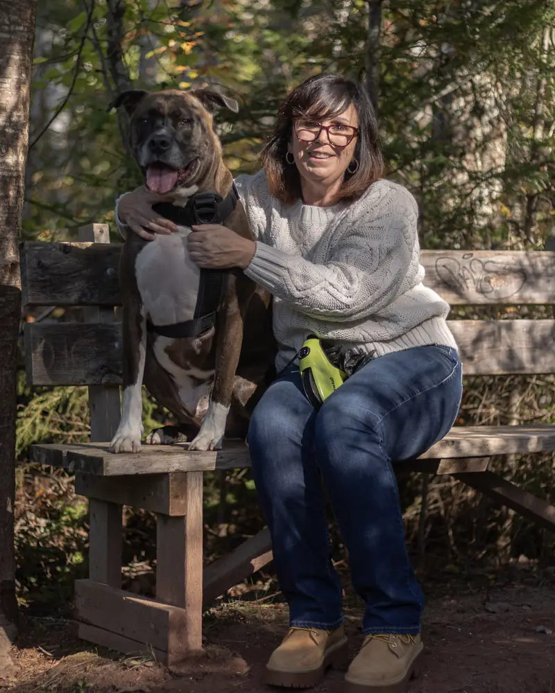 Kim sitting on a wooden trail bench with her arm around Frankie